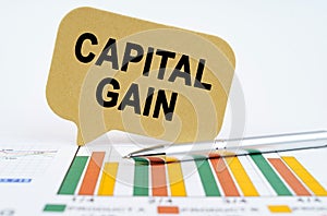 On the financial charts lies a pen and a sign with the inscription - capital gain