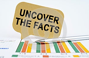 On the financial charts lies a pen and a sign with the inscription - Uncover the Facts