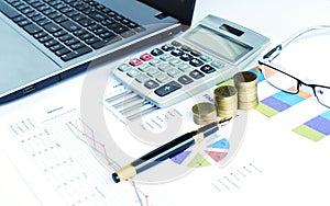 Financial concept with coins stack and calculator and fountain pen and eyeglasses and labtop on document chart data backgrounds