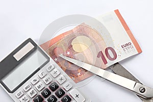 Financial concept: cut the debt. a ten euro bill, a pair of scissor and a calculator on white background with copy space