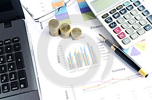 Financial concept with money coins stack and business fountain pen and calculator and eyeglasses and labtop with document chart on