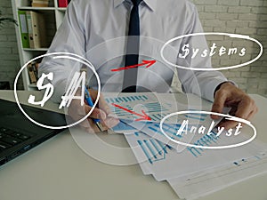 Financial concept about SA Systems Analyst with handwritten abbreviation.Busy businessman under stress due to excessive work on