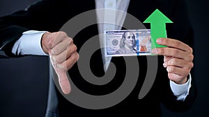 Financial consultant with dollar banknotes showing thumbs down and green arrow