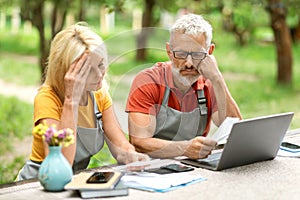 Financial Crisis. Upset Mature Farmers Couple Checking Bills With Laptop In Garden