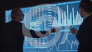 Financial data analysts analyzing charts on big screen