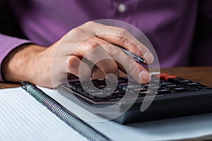 Financial data analyzing. Close-up photo of a businessman`s hand writing and counting on calculator in office