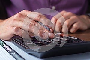 Financial data analyzing. Close-up photo of a businessman`s hand writing and counting on calculator in office