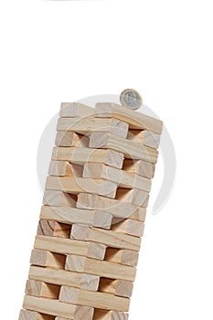 Toy wooden blocks tower with a 1 euro coin on the top inclined until falling isolated on white background with copy space