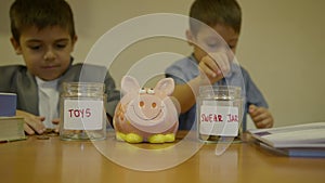 Financial education. Children savings. Boys sorting coins between toys savings and swear jar with piggy bank in the