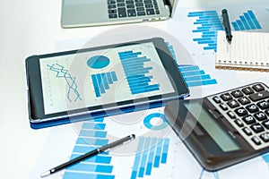 Financial graph chart on digital mobile tablet, laptop computer, calculator, business document on workplace desk