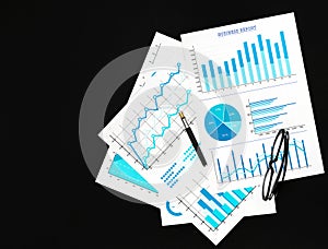 Financial graphs with pen and eyeglasses on the black background. Top view. Copy space