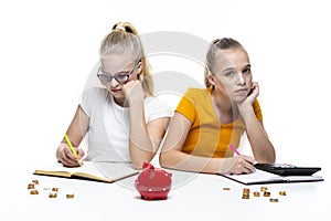 Financial Ideas and Concepts. Portrait of Caucasian Teenager Twin Girls Posing With Coins and Piggy Bank. Making Notes with