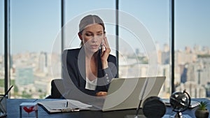 Financial manager talking smartphone at desk. Young businesswoman working laptop