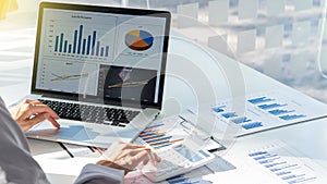 Financial market analyst, a young woman working in a sunny office on a laptop while sitting at a wooden table, a businessman