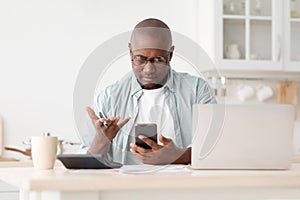 Financial problem. Angry african american man calculating utility charges and bills, using calculator and phone