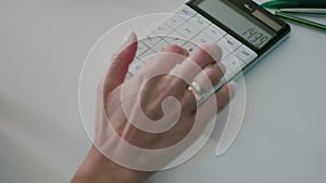 Financial reports. Close-up female hand counting on a white calculator