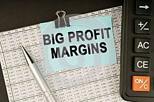 On financial reports lies a calculator, a pen and a sticker with the inscription - Big Profit Margins