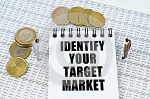 On financial reports there are figurines of people, coins and a notepad with the inscription IDENTIFY YOUR TARGET MARKET
