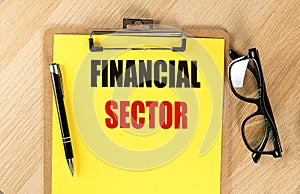 FINANCIAL SECTOR text on yellow paper on clipboard with pen and glasses