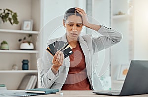 Financial stress, concerned and frustrated woman holding bank cards in her hand at her desk. Business female worried