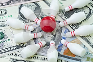 Financial success target concept, red winning bowling strike ball surround with knocked down pins on pile of US dollar banknotes