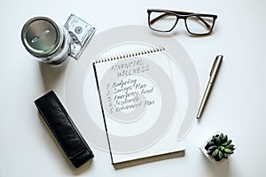 Financial Wellness. Open notepad with text Financial Wellness and list on table with mason jar saving bank, stationery