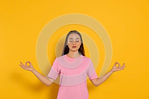 Find zen. Beautiful young woman meditating on yellow background