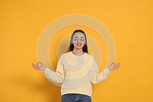 Find zen. Beautiful young woman meditating on yellow background