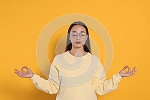 Find zen. Beautiful young woman meditating on yellow background