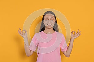 Find zen. Beautiful young woman meditating on yellow background