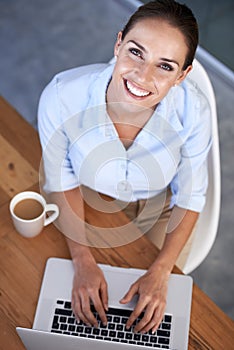 Finding business solutions online. High angle portrait of a young businesswoman sitting with her laptop and a coffee.