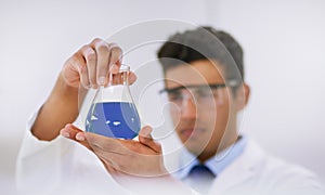 Finding cures in the lab. a lab technician examining a beaker of blue liquid while standing in a lab.