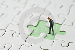 Finding the missing piece for business success concept, miniature people businessman standing and looking at the missing white