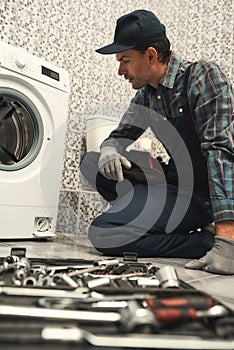 Finding a solution. Plumber repairing washing machine