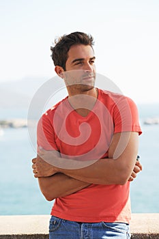 Finding time to get away from it all. A handsome young man leaning against a wall with a view of the ocean in the