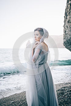 Fine art photo of a beautiful woman in a delicate gray dress on the beach in the summer