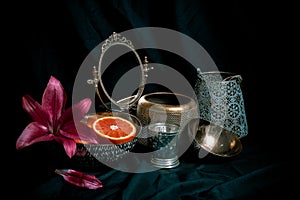 Fine art style low key still life with antique decor items on dark background. Composition of vases, flowers, mirror, orange with photo