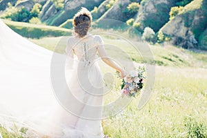 Fine art wedding photography. Beautiful bride with bouquet and dress with train in nature