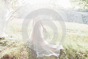 Fine art wedding photography. Beautiful bride with shoes and dress with train against the sunin nature