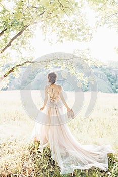 Fine art wedding photography. Beautiful bride with shoes and dress with train against the sunin nature