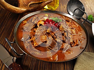 Fine Meat - Wild Game Meat Goulash in a Pan with Cranberries on wooden Background