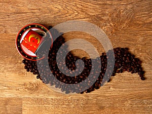 A fine porcelain ware tea coffee cup in red, black and yellow moon, spilled coffee beans on oak wood rustic background.