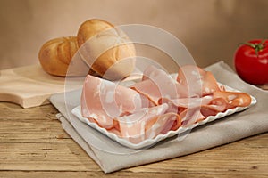 fine slices of mortadella on a white plate. italian sausage on a wooden table with tomatoes and bread.