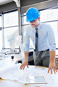 Fine tuning his design. an architect wearing a safety helmet and examining blueprints.