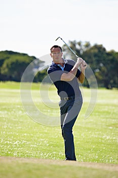 Fine tuning his follow through. a handsome mature man playing a game of golf.