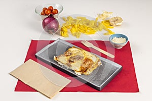 Fine veal lasagna with cheese and bÃ©chamel gratin on a black plate and red tablecloth