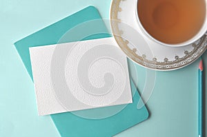 Fine white porcelain china cup with tea, teal pencil, white note card and aqua mint blue background