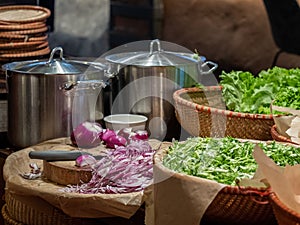 Finely chopped red onion and a cook knife on a cutting board. Nearby are large pots and baskets with salad leaves