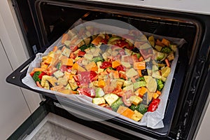 Finely chopped and seasoned vegetables on a baking sheet lined with baking paper in the oven. Potatoes, bell peppers, squash,