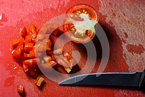 Finely chopped tomato with knife on a red rough chopping board